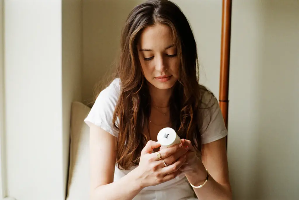 A person in a white shirt is seated, examining a white cylindrical object with a thoughtful expression.