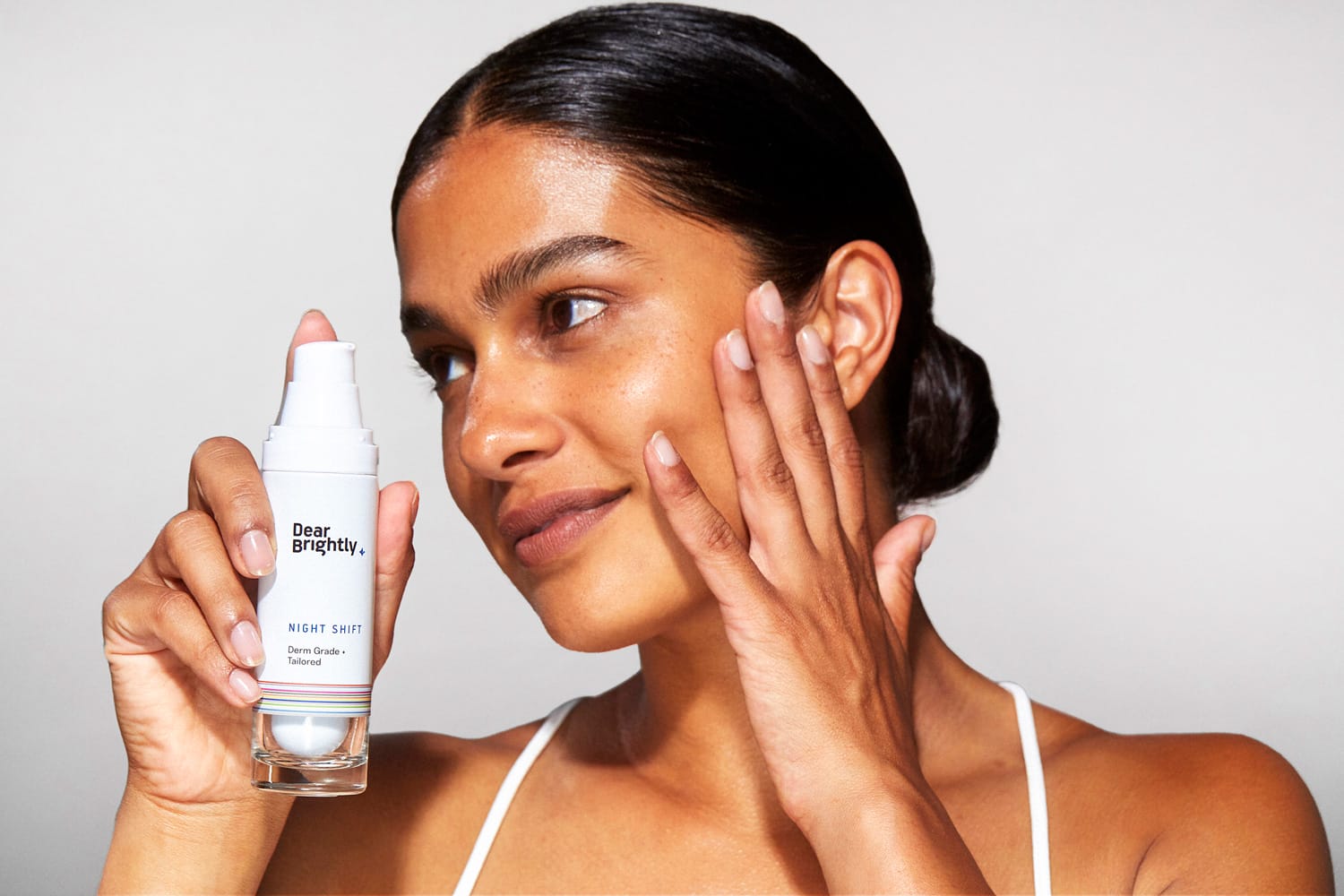 A women with her hand on her face holding a bottle of Dear Brightly's Night Shift