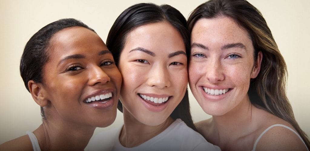Three people smiling, standing close together against a neutral background.