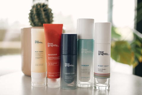 Five skincare products from Dear Brightly, including Wild Thing, Never Skip, Liquid Calm, Sunshift, and Night Shift, displayed in a row on a table.